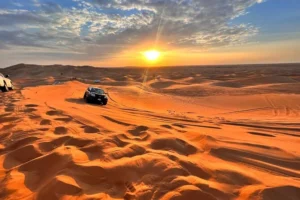 Morning desert safari Dubai with tourists on camels during sunrise in red sand dunes 